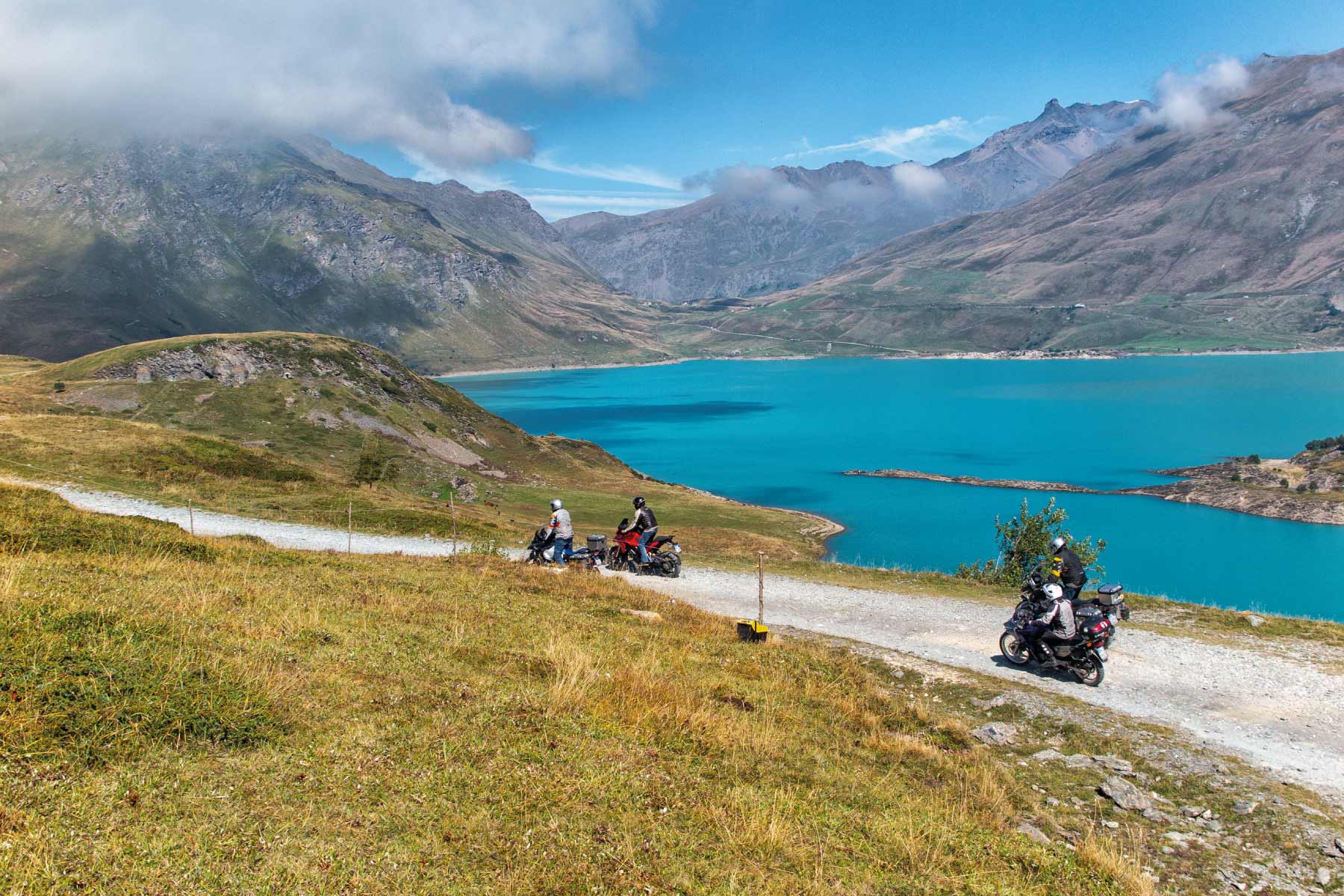 Motociclisti in viaggio su sentiero con vista lago turchese e montagne.