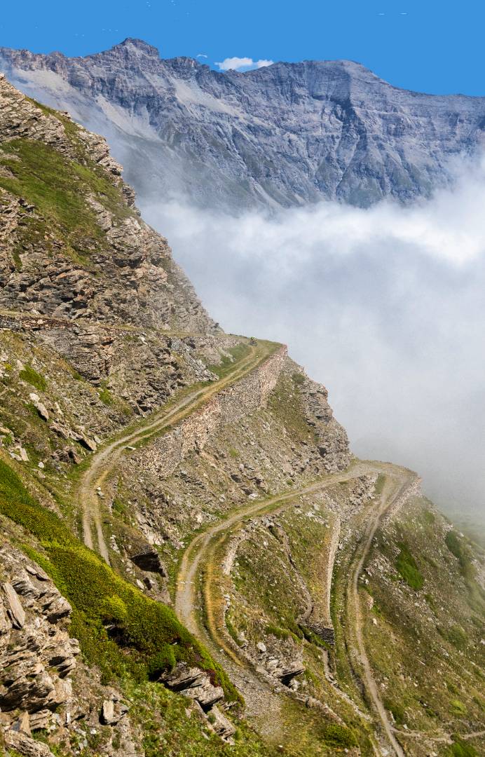 Serpentine di una strada di montagna con nuvole basse e vette rocciose.