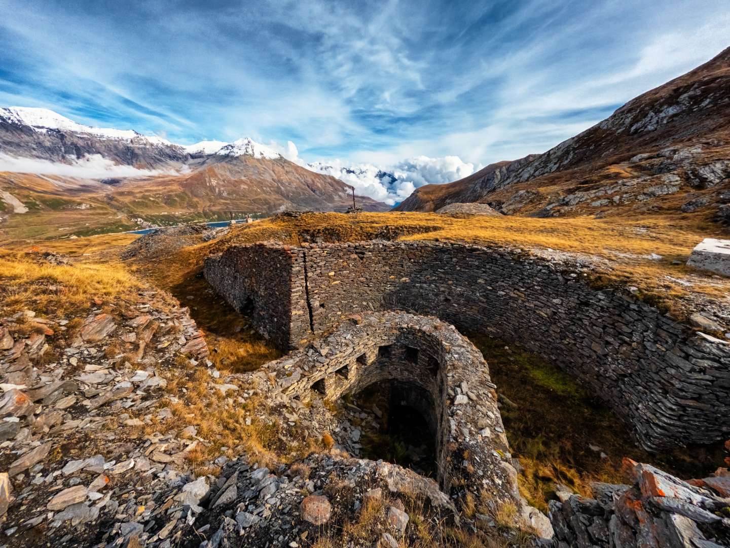 Rovine di costruzioni in pietra in primo piano con montagne innevate sullo sfondo.