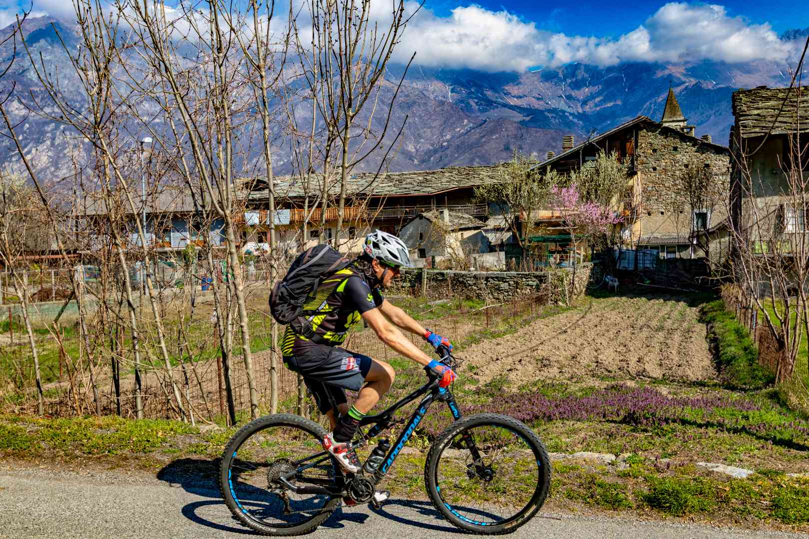 Ciclista su strada vicino a vecchie case di montagna e vegetazione spoglia.