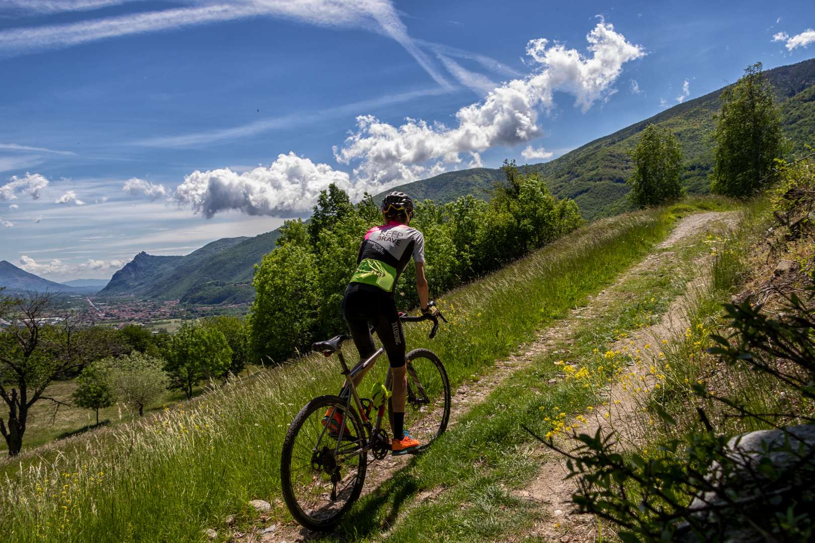 Ciclista su sentiero collinare con vista su montagne e cielo nuvoloso.