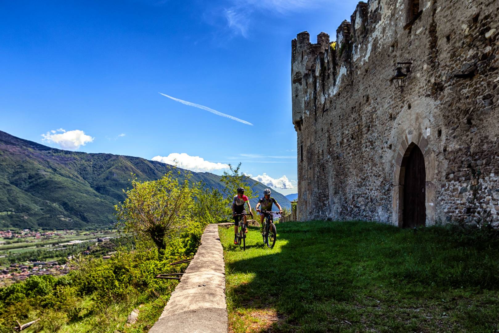 Ciclisti pedalano accanto a rovine storiche con vista panoramica sulle montagne.